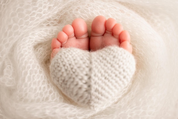 Le petit pied d'un nouveau-né Pieds doux d'un nouveau-né dans une couverture en laine blanche Gros plan sur les talons et les pieds d'un nouveau-né Coeur blanc tricoté dans les jambes d'un bébé Macro photographie