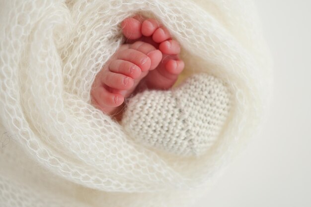 Le petit pied d'un nouveau-né, les pieds doux d'un nouvellement-né dans une couverture de laine blanche, le gros plan des orteils, des talons et des pieds d'un nouveauné, le cœur blanc tricoté dans les jambes d'un bébé, la photographie macro.