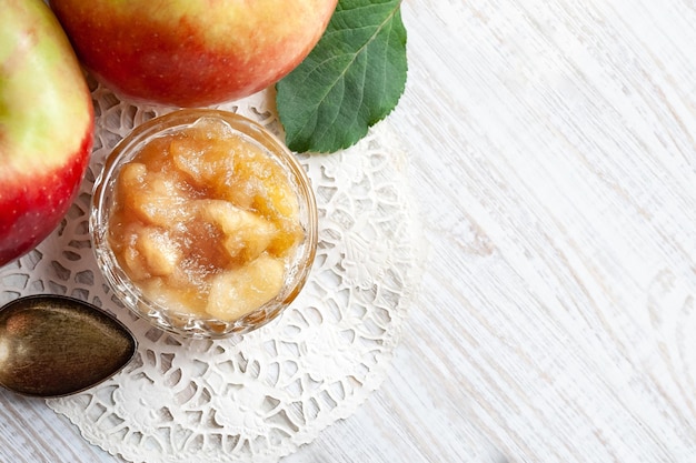 Petit plat avec de la confiture de pommes avec des pommes entières et une cuillère sur une table en bois blanc mise au point sélective