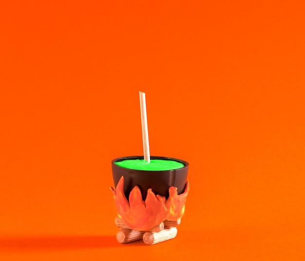 Le petit pot de sorcière avec potion est cuit au feu sur fond orange affiche minimale d'Halloween