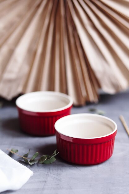 Petit ramequin en céramique émaillée. Tasse de cuisson rouge pour cupcakes, muffins sur fond gris et blanc. Plat de cuisson en céramique.