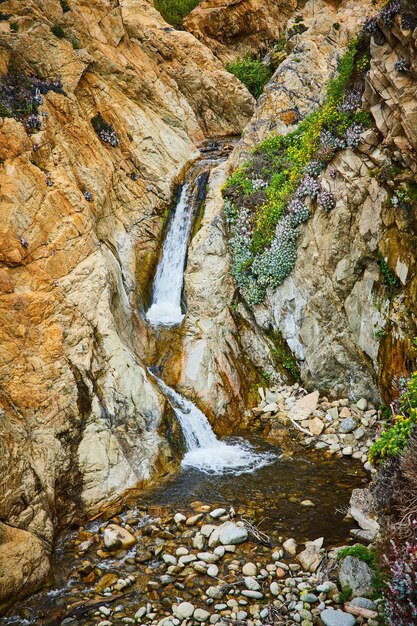 Petit ruisseau entre les parois de la falaise qui se jette dans un bassin d'eau peu profond avec de grandes pierres