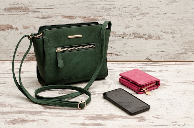 Petit sac femme vert, sac à main et téléphone sur un bois