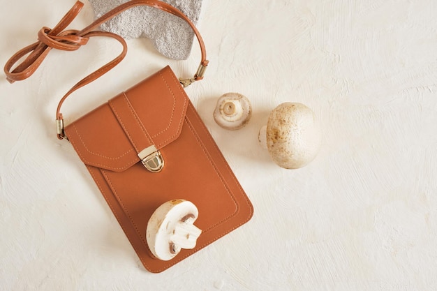 Petit sac marron pour smartphone et cartes de crédit et champignons sur fond beige, concept en cuir végétalien