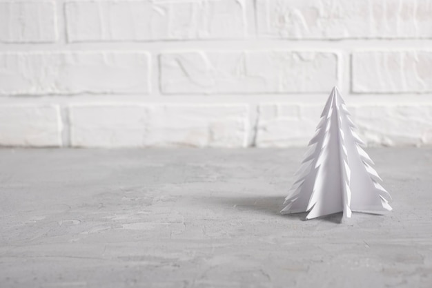 Petit sapin de Noël blanc en papier sur fond de briques claires pour le nouvel an dans un style scandinave avec espace de copie