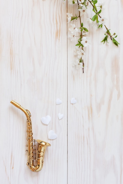 Petit saxophone doré, figurines en forme de cœur blanc et branches de cerisier en fleurs.