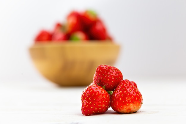 Petit tas de fraises avec bol en bois en arrière-plan