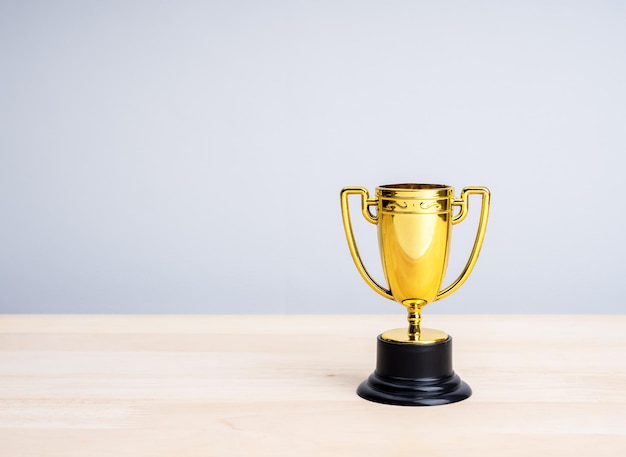Un petit trophée en or, double poignée en laiton et en acier isolé sur une table en bois et un fond blanc avec un espace de copie Trophée d'or sur le bureau minimal Récompense du succès, récompense de l'effort et concept de prix gagnant
