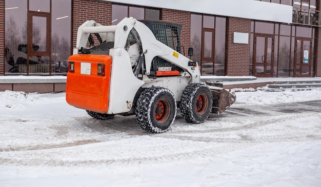 Petit véhicule de déneigement enlevant la neige sur la place de la ville Tracteur jaune ou orange nettoyant la neige