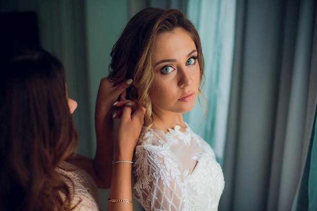 Petite amie met une mariée boucle d'oreille. Jeune femme. Fille en robe de mariée et avec mariage met