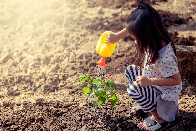 Petite asiat arrosant le jeune arbre avec arrosoir dans le ton de couleur vintage