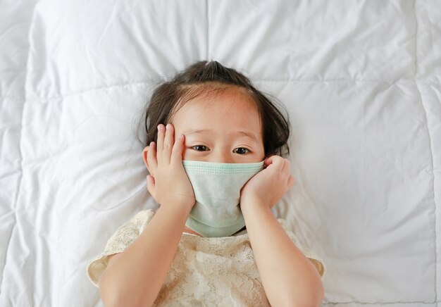 Petite asiat portant un masque de protection allongé sur le lit.