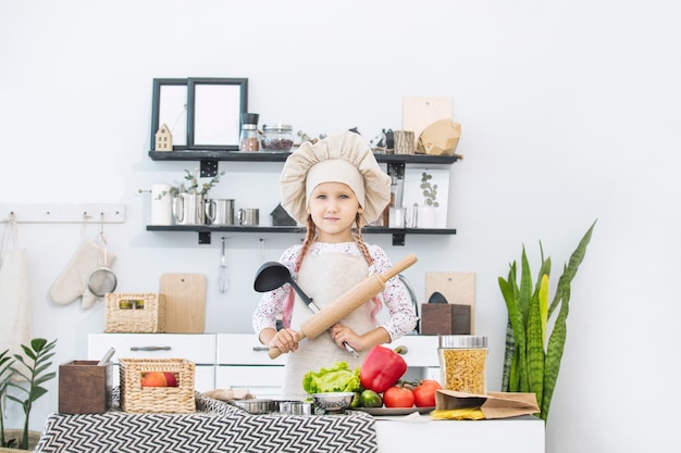 Petite belle enfant fille cuisiner dans la cuisine avec différents légumes et spaghettis