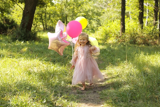 une petite belle fille blonde vêtue d'une robe rose avec des ballons se promène dans le parc