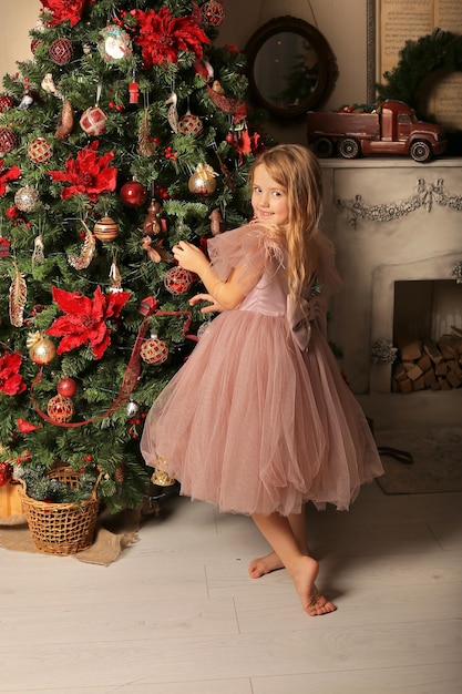 une petite belle fille blonde vêtue d'une robe rose décore le sapin de Noël