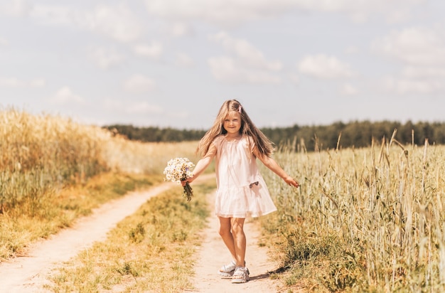 Une petite belle fille avec un bouquet de marguerites dans un champ de blé