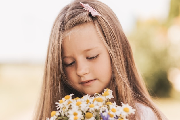 Une petite belle fille avec un bouquet de marguerites dans un champ de blé
