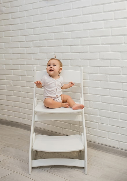 petite belle fille est assise sur une chaise de plus en plus dans un body blanc