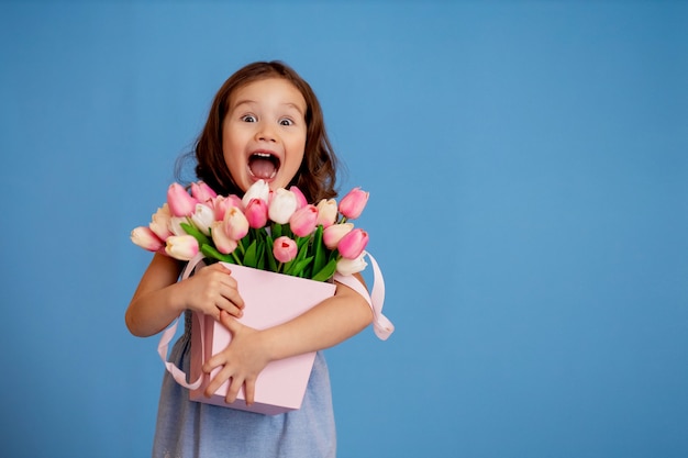 Petite belle fille sur fond bleu avec un bouquet de tulipes
