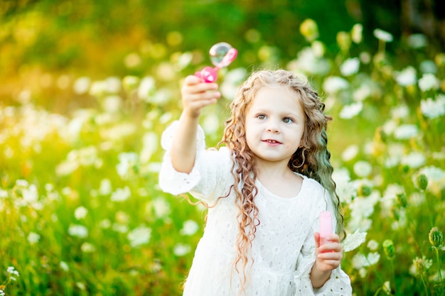 petite belle fille jouant sur la pelouse en été avec des bulles de savon.