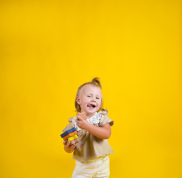 petite belle fille avec un jouet pyramide se dresse et montre sa langue sur fond jaune