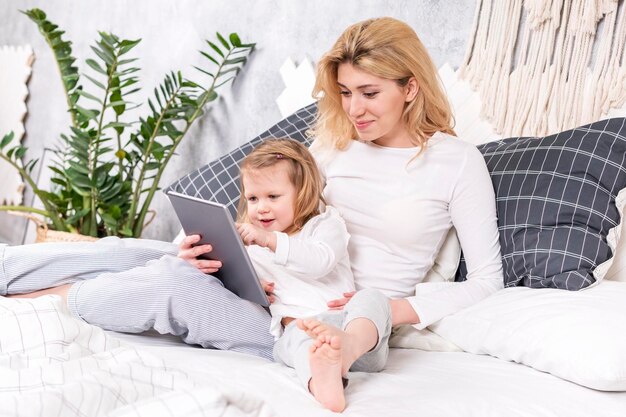 petite belle fille montre le doigt de sa mère sur la tablette, assise sur le lit