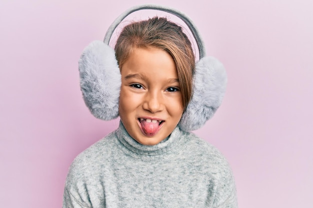 Petite belle fille portant un cache-oreilles moelleux qui sort la langue heureuse avec une drôle d'expression