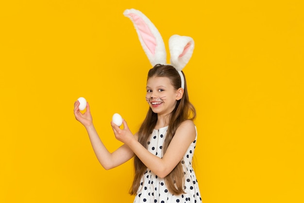 Une petite belle fille se prépare pour les vacances de Pâques et s'habille comme un lapin de Pâques et prend des œufs de poule pour les décorer Une fille en costume de lapin de Pâques sur fond jaune isolé