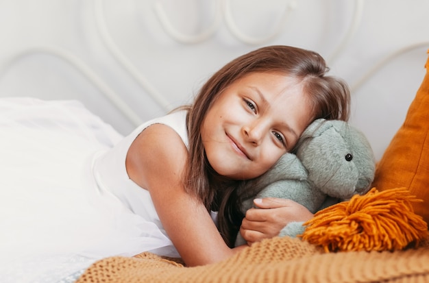 Petite belle fille se trouve sur un lit et embrasse un lièvre en peluche doux