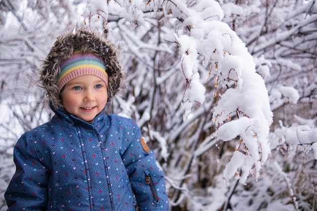 Petite belle fille en vêtements d'hiver, seule au milieu d'une forêt enneigée