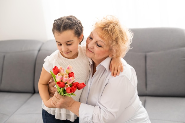 Petite belle petite-fille donne à sa grand-mère un bouquet de tulipes roses. Le concept de famille, respect, génération, mère, éducation.