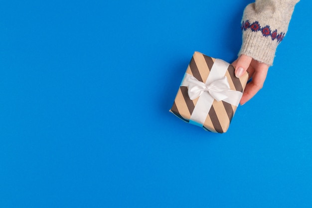 Petite boîte cadeau dans les mains féminines sur fond bleu, vue d'en haut