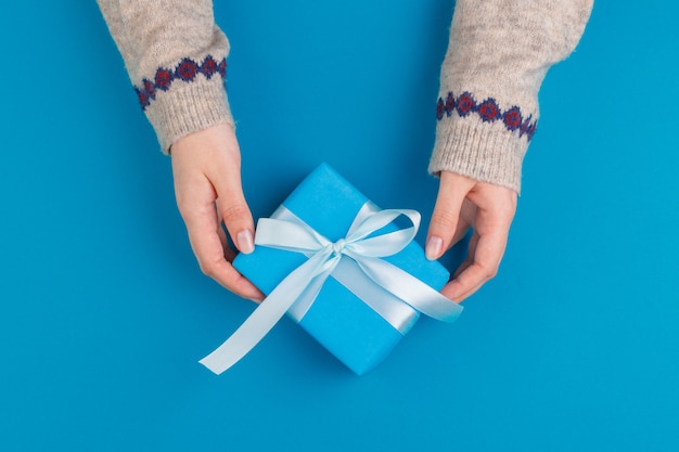 Petite boîte cadeau en mains féminines sur fond bleu, vue de dessus