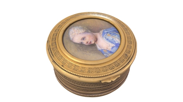 Une petite boîte ronde en or avec le portrait d'une jeune fille dessus.