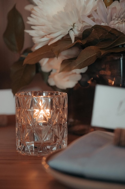 Une petite bougie en verre est posée sur une table près d'une assiette et d'une serviette.