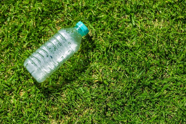 Petite bouteille d&#39;eau froide reposant sur un terrain herbeux vert par une journée chaude et ensoleillée