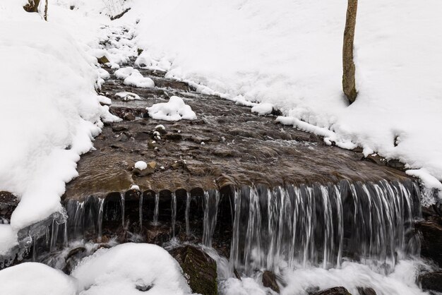 Petite cascade de montagne d'écoulement d'eau glacée parmi les pierres humides couvertes de neige blanche