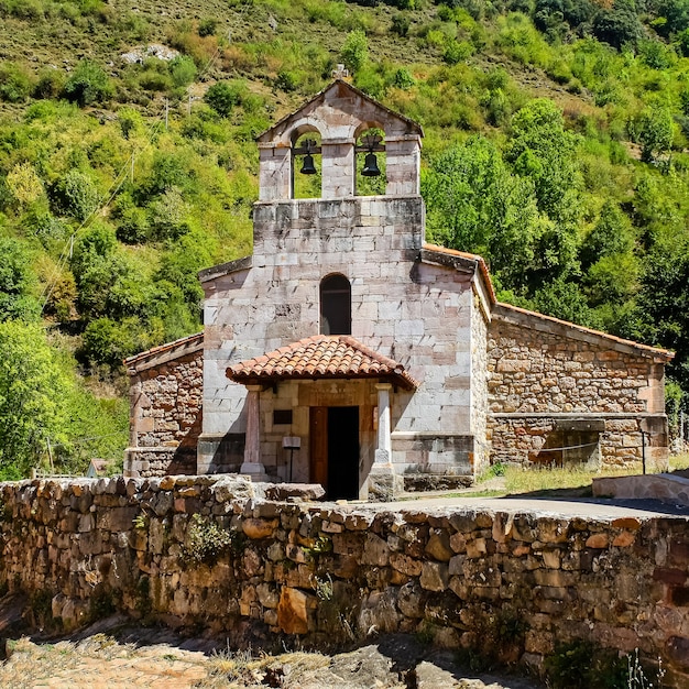 Petite chapelle en pierre à côté de l'ancien mur de pierre dans le champ vert. Asturies Espagne.