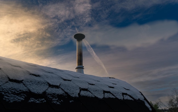 Une petite cheminée de sauna en fer avec de la fumée contre le ciel en hiver