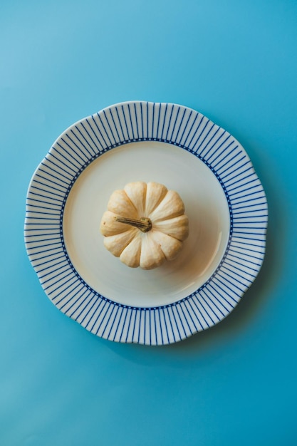 Une petite citrouille blanche sur une grande assiette sur fond bleu