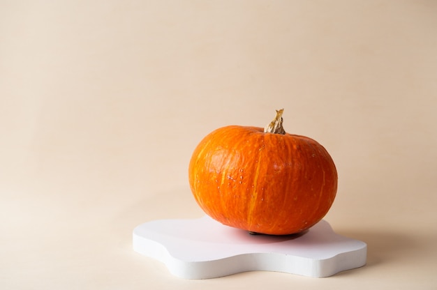 Petite citrouille orange sur fond beige pastel avec espace de copie. Célébration de concept d'Halloween ou de Thanksgiving. Podium de cosmétiques pour halloween. Automne nature morte.