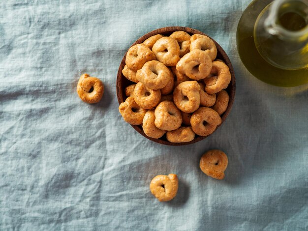 Photo petite collation italienne traditionnelle taralli ou tarallini dans un bol en bois sur fond de serviette de lin bleu clair aperitif rustique de taralli avec espace de copie vue de haut ou à plat