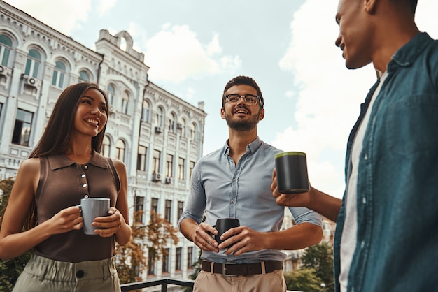 Petite conversation de jeunes collègues positifs en tenue décontractée tenant des tasses et discutant de quelque chose tout en