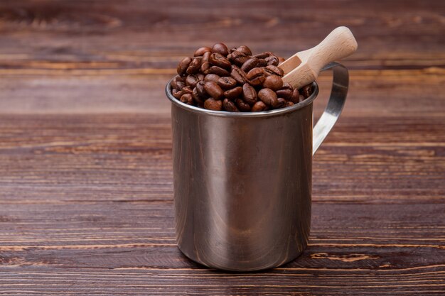 Petite cuillère en bois dans une tasse en acier avec des grains de café