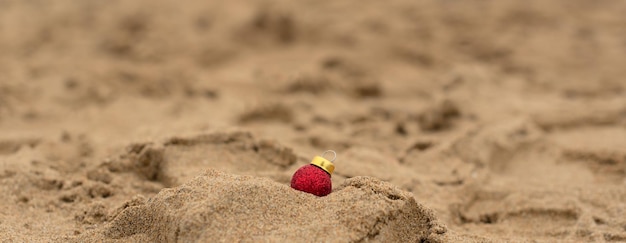 Petite décoration de boule de Noël rouge sur fond de sable de plage jaune Noël ou Nouvel An avec espace de copie et mise au point sélective Vacances de vacances dans les tropiques ou les pays exotiques pendant le concept de Noël