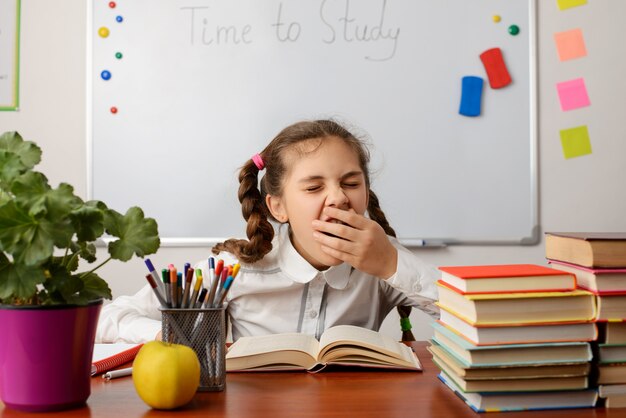 Petite écolière bâillant en lisant un livre