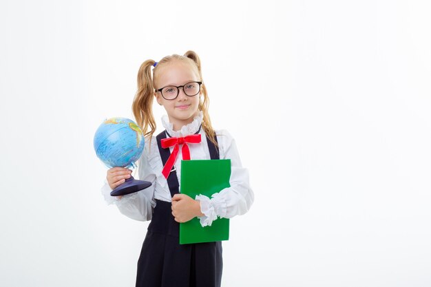 Une petite écolière dans un uniforme scolaire tient un globe isolé sur fond blanc