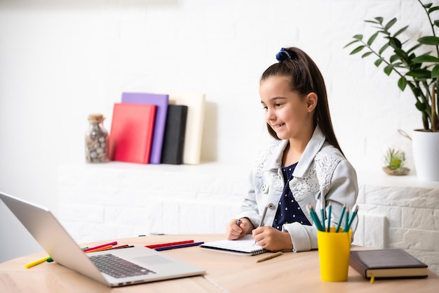 Petite écolière devoirs d'étudiant sur fond argenté d'ordinateur portable