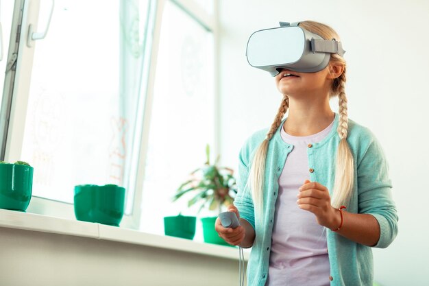 Petite écolière portant de grandes lunettes VR impressionnée en jouant à des jeux virtuels à l'école