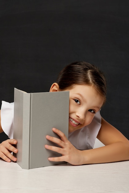 La petite écolière regarde de derrière le livre